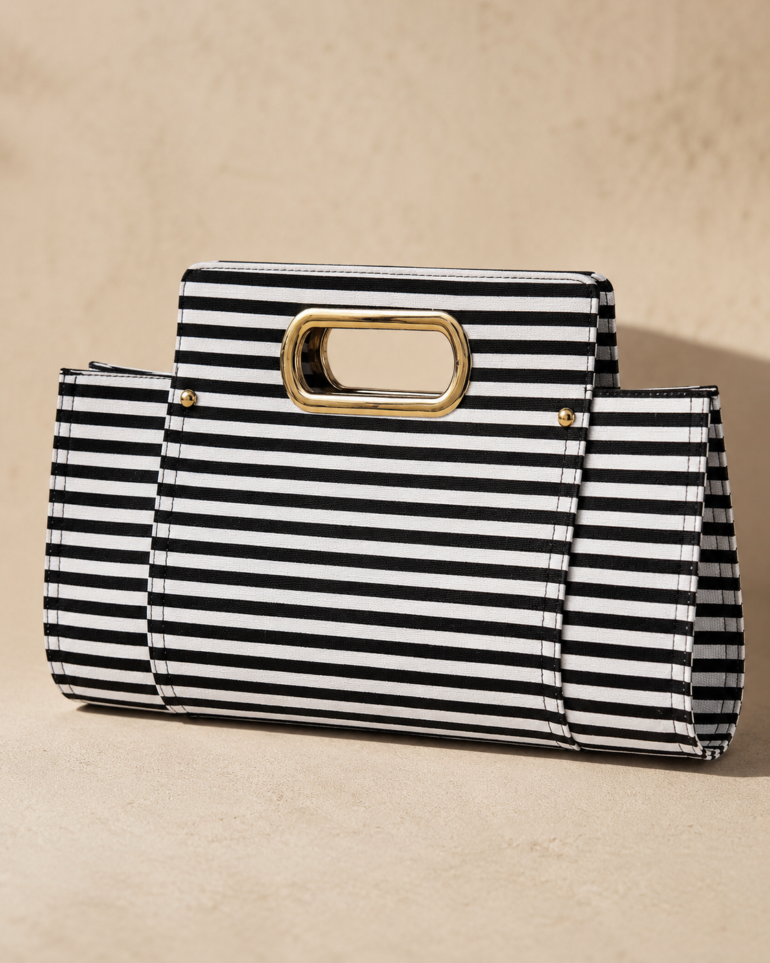 Black and white striped clutch with a gold handle on a beige background