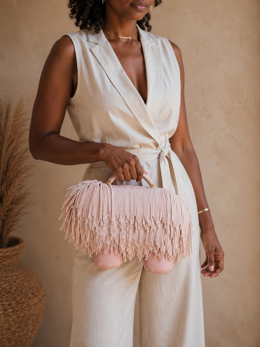 Woman holding a pink fringed handbag against a beige background