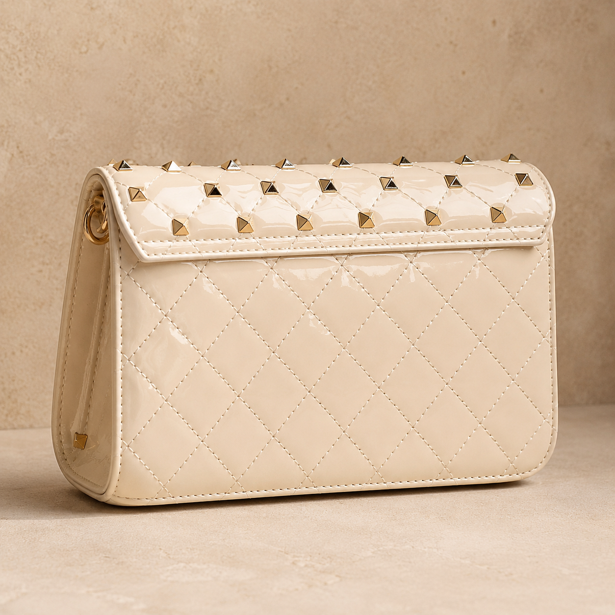 Beige quilted handbag with gold studs on a beige background