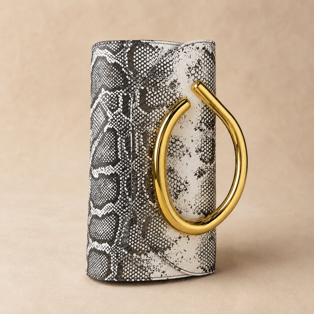 Clutch bag with snake skin pattern and gold handle on a beige background