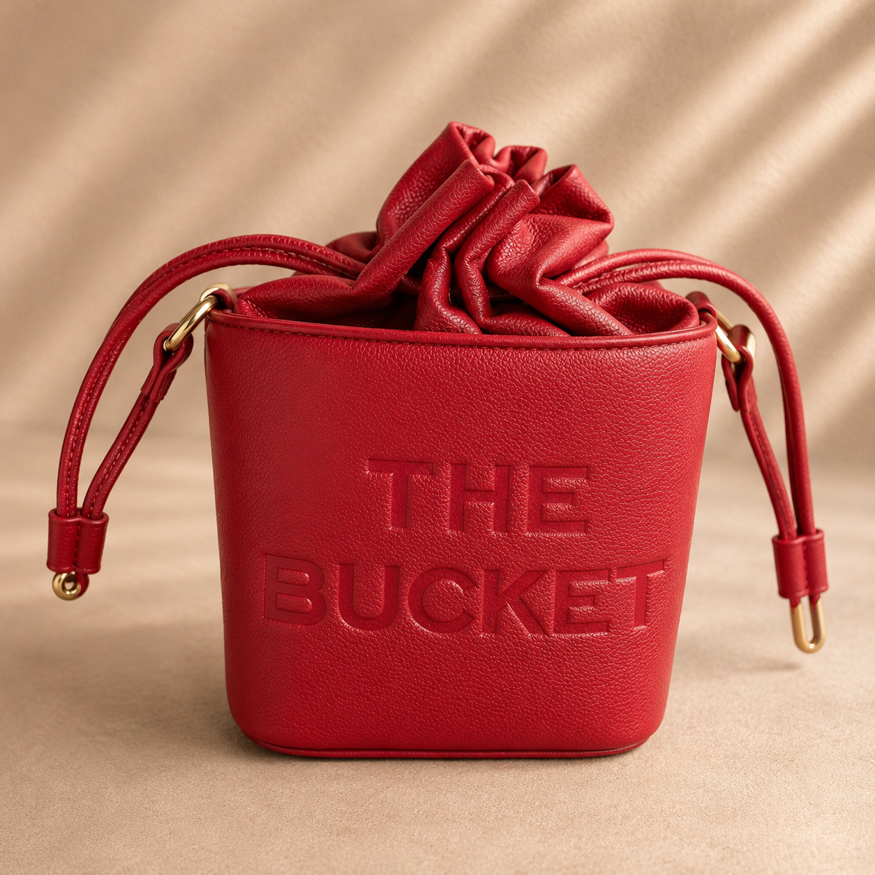 Red leather bucket bag with 'THE BUCKET' embossed on a beige background