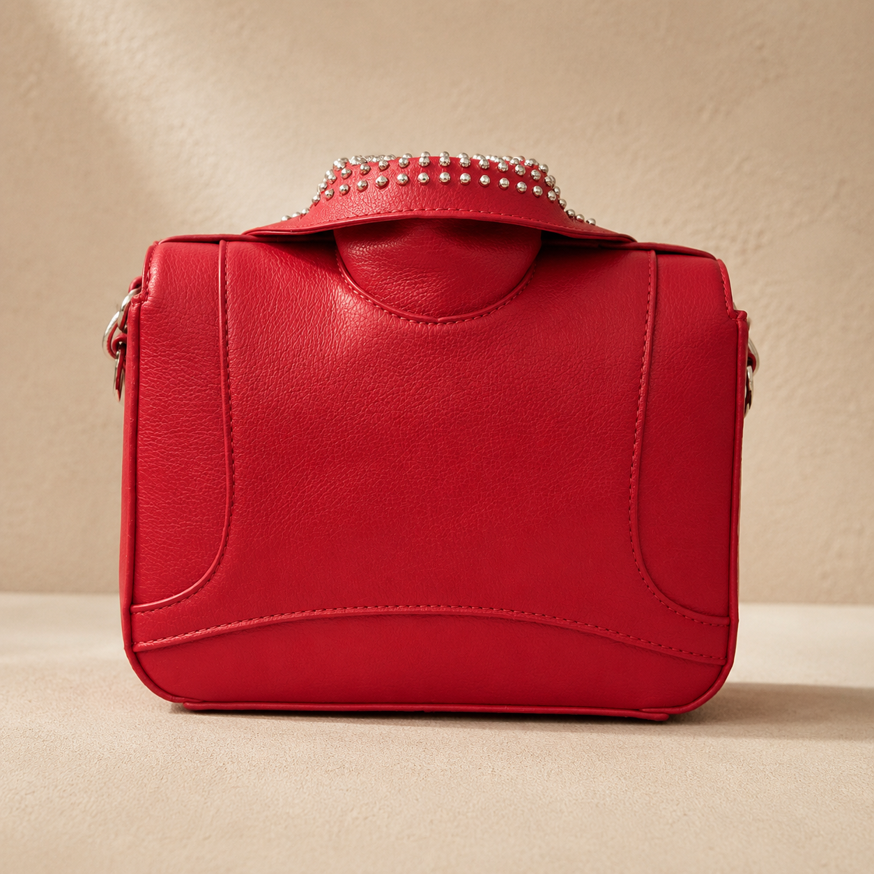 Red handbag with studded detail on a beige background