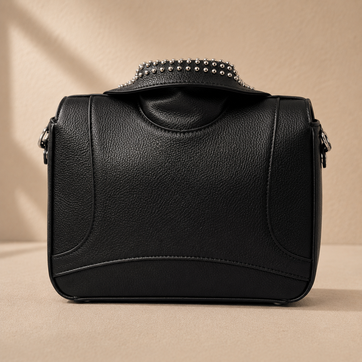 Black leather handbag with studded detail on a beige background