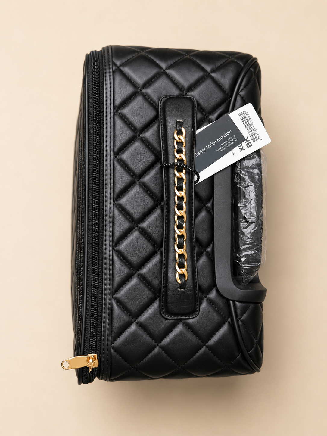 Black quilted handbag with gold chain detail on a beige background