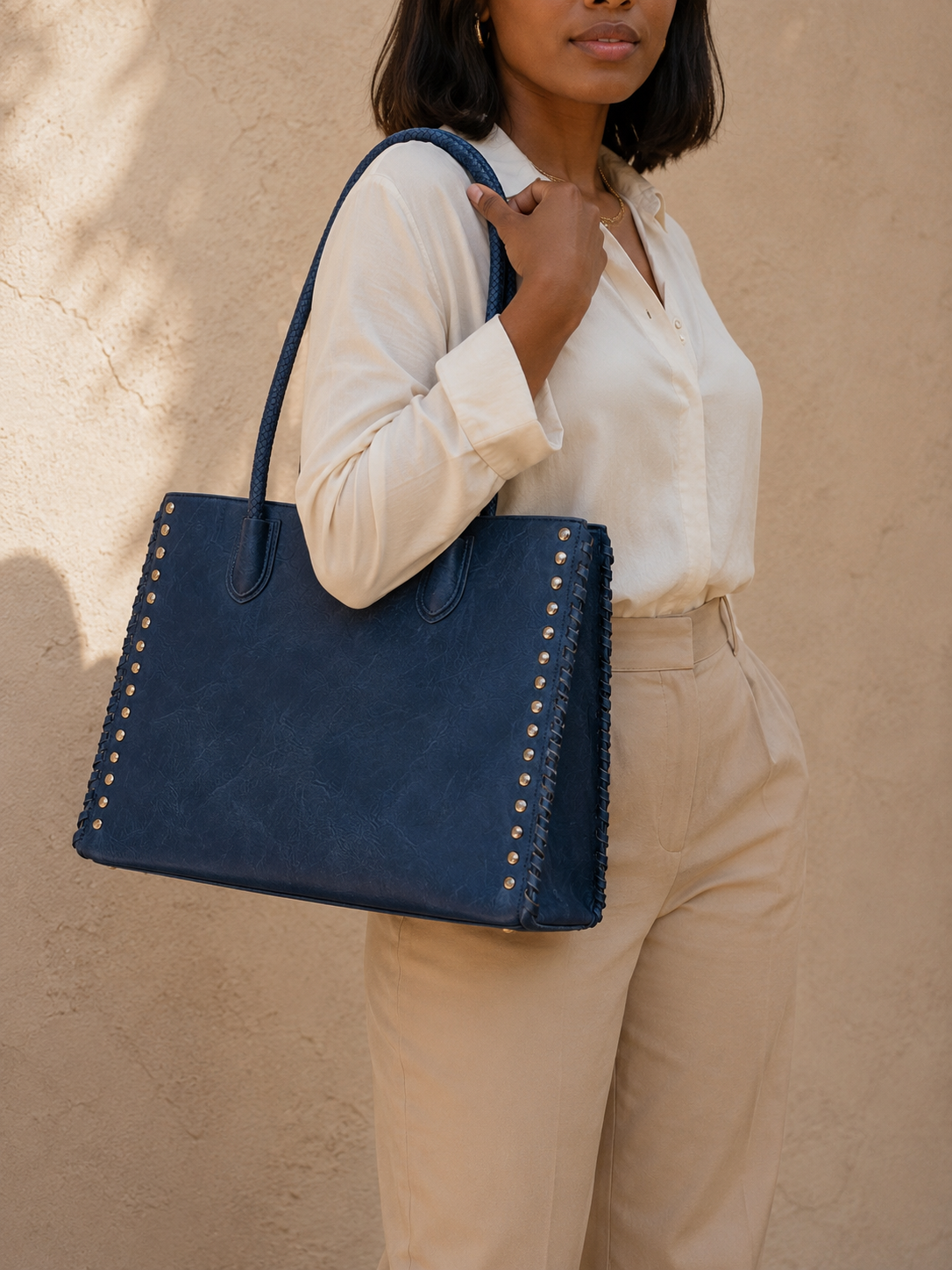 Woman holding a navy blue studded tote bag against a beige background