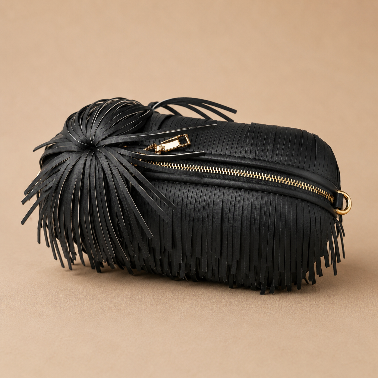 Black fringed handbag with gold zipper on a beige background