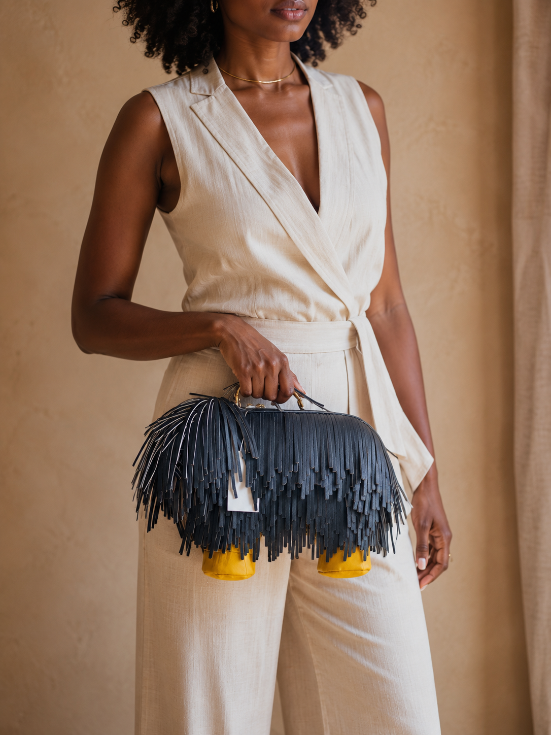 Woman holding a black fringed handbag with yellow bottom against a beige background
