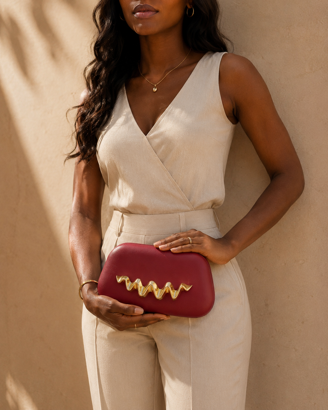 Woman holding a red clutch with gold accents against a beige background